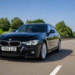 Czarny sedan BMW serii 3 jedzie autostradą w słoneczny dzień