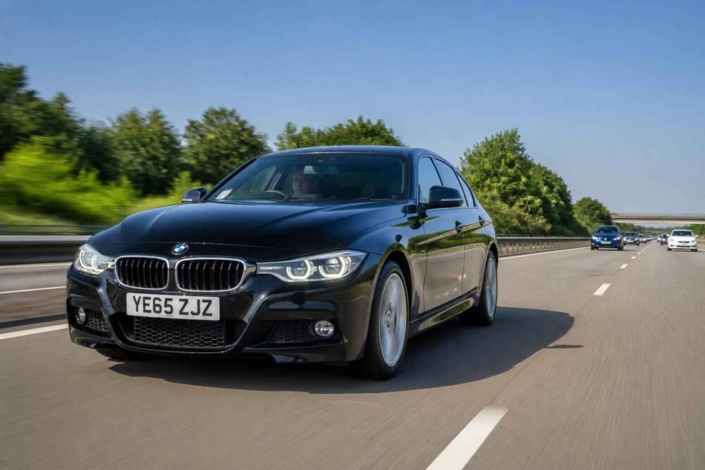 Czarny sedan BMW serii 3 jedzie autostradą w słoneczny dzień