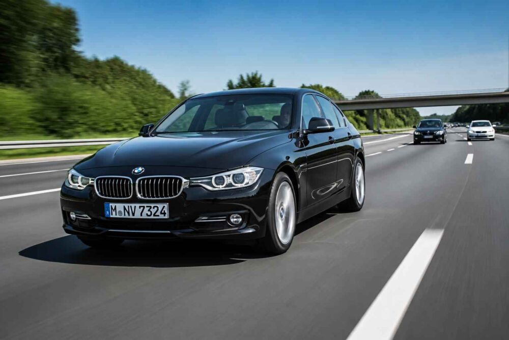 Czarny BMW serii 3 podczas jazdy autostradą Czarny sedan BMW serii 3 porusza się prawym pasem autostrady pod wiaduktem